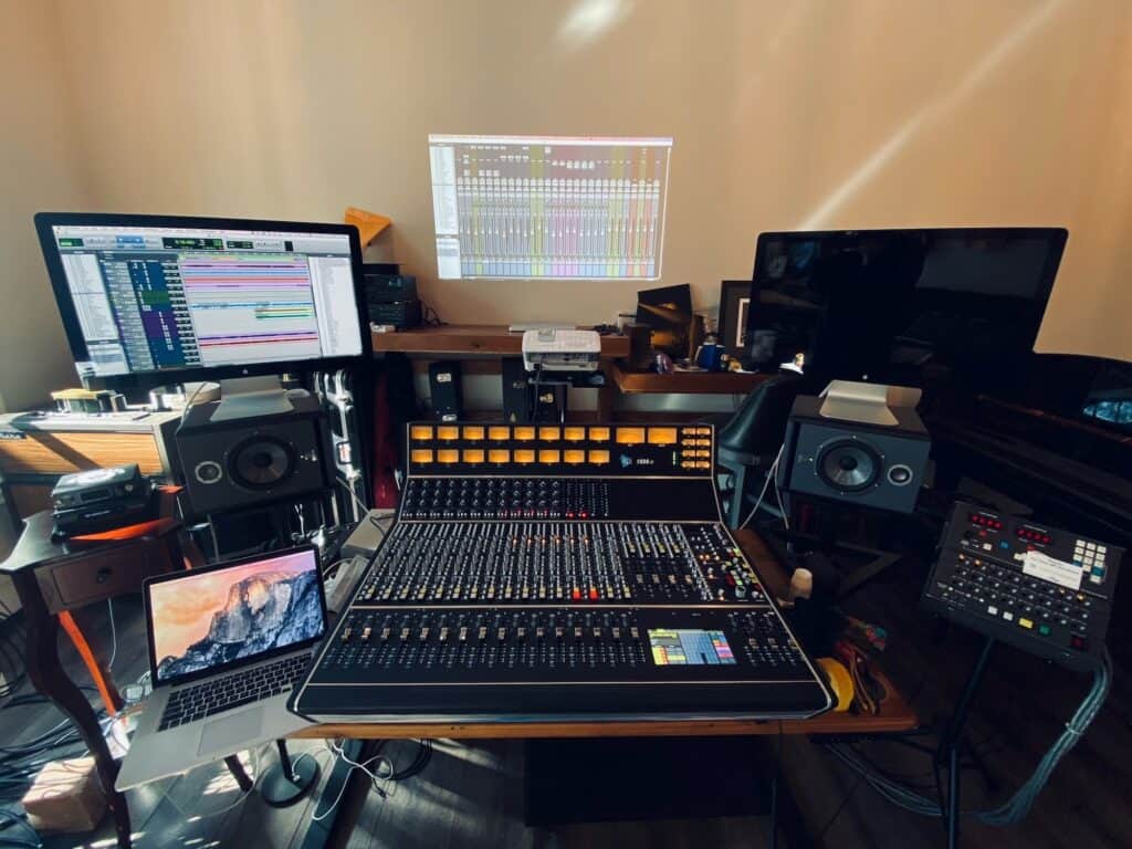 Photo of API 1608 Mk2 recording console in a home studio environment with displays to the left and right